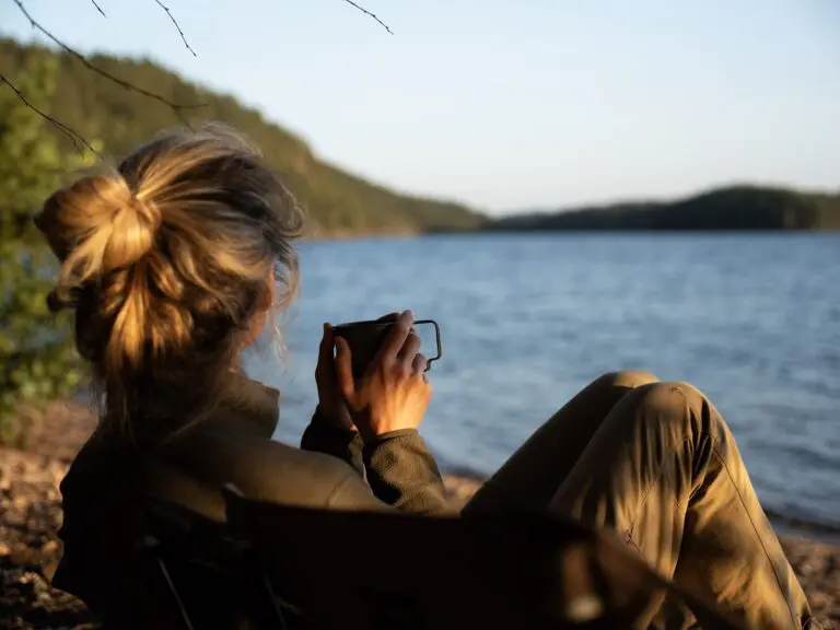 femme buvant un café au bord d’un lac au coucher du soleil