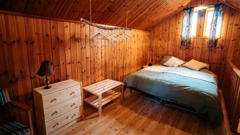 chambre chaleureuse dans une cabane en bois, avec un lit, une commode et des cintres