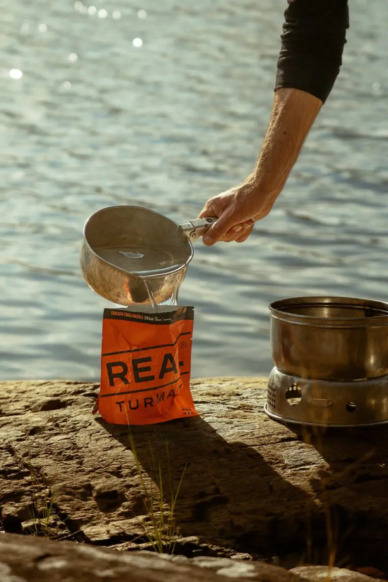 personne versant de l’eau dans un sachet de repas déshydraté au bord d’un lac