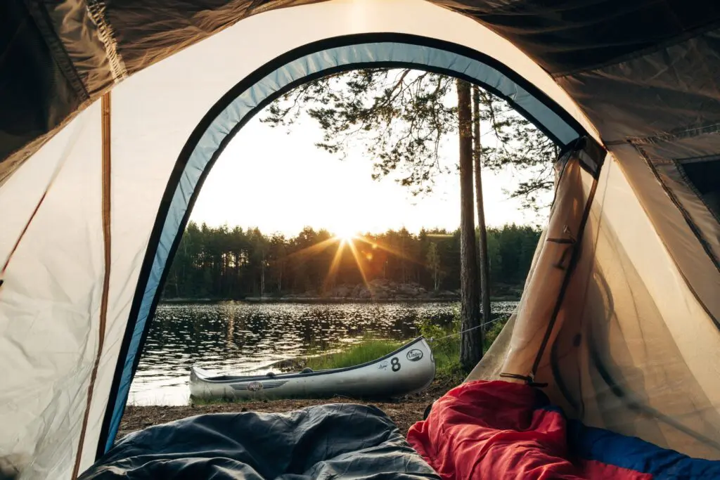 vue depuis une tente sur un lac, une forêt et un canoë au coucher du soleil