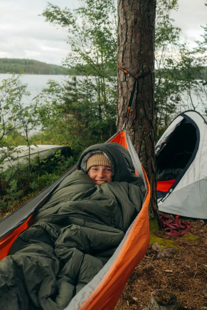 person smiling in hammock by lake with tent