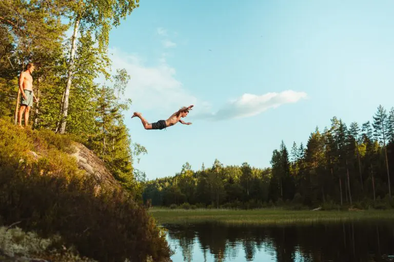 homme sautant d’une falaise dans un lac sous le regard d’un ami