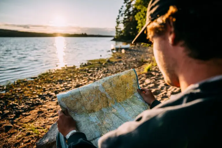 personne en casquette lisant une carte au bord d’un lac au coucher du soleil