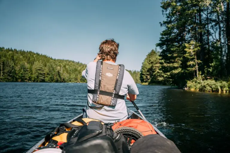 personne pagayant en canoë sur un lac entouré de forêt