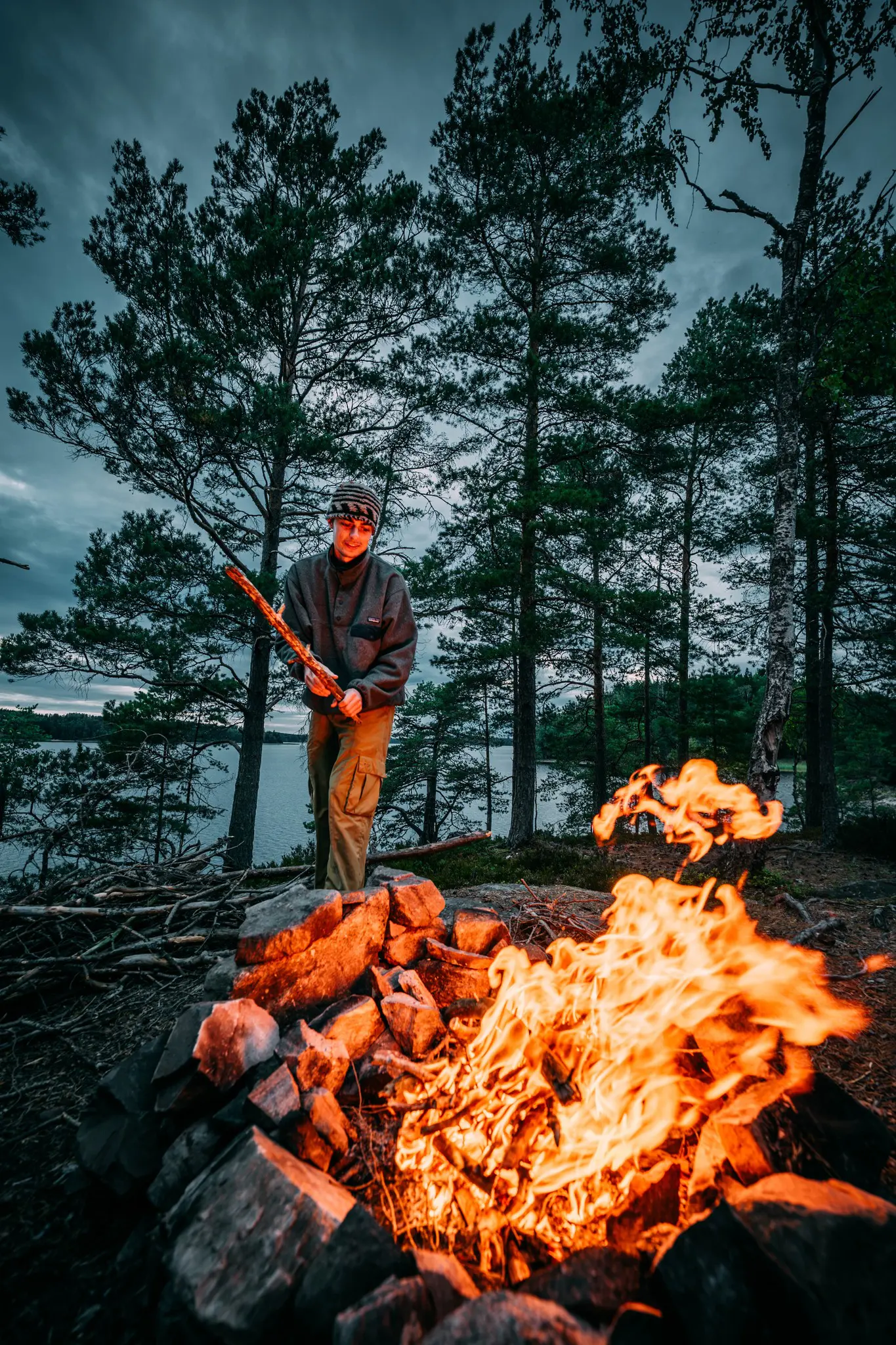 personne entretenant un feu de camp au bord d’un lac dans une forêt