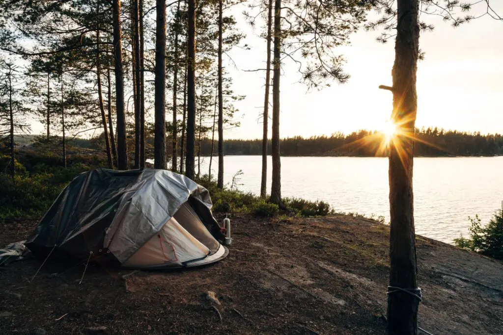 tente au bord d’un lac, dans une forêt au coucher du soleil