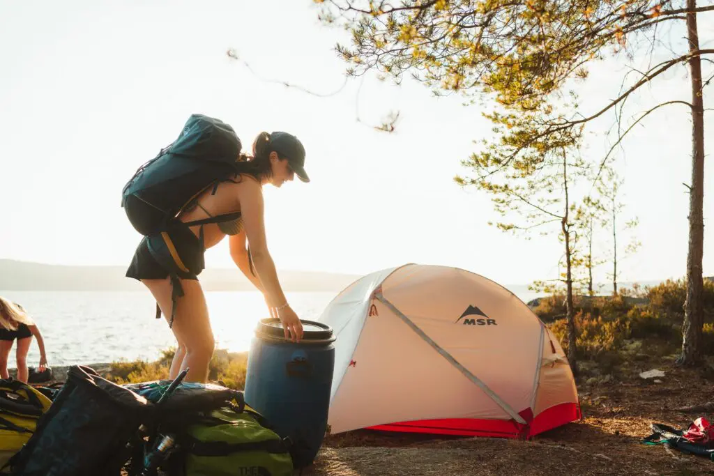 femme installant son campement au bord d’un lac avec une tente et un sac à dos
